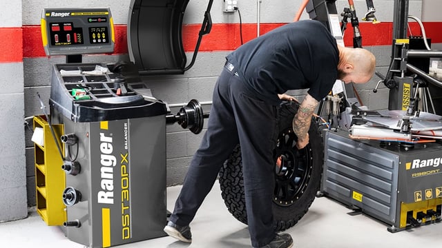 Commercial rim-clamp tire changer with pneumatic assist tower alongside a computerized wheel balancer