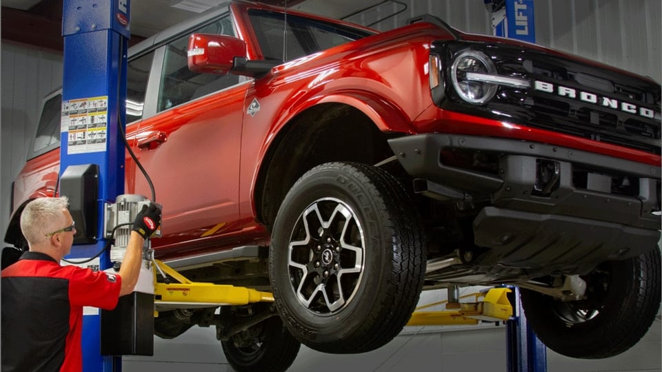 Heavy-duty commercial pickup elevated on a red two-post hydraulic lift inside a sunlit West Texas repair bay